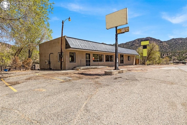 view of front of house with stucco siding, uncovered parking, a mountain view, and metal roof