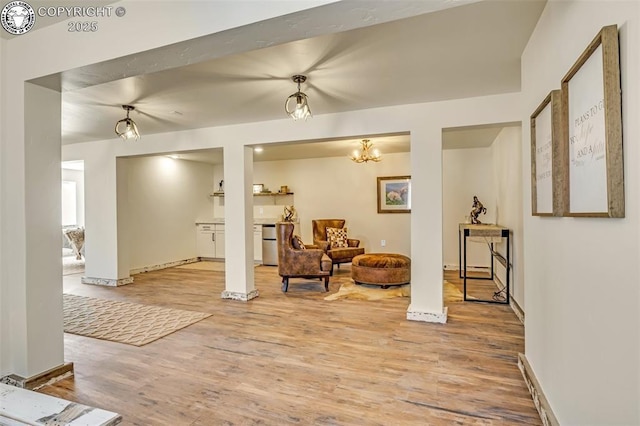 living area with a notable chandelier, light wood-style flooring, and baseboards