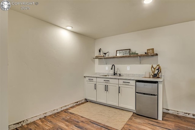 bar with light wood finished floors, baseboards, wet bar, fridge, and a sink