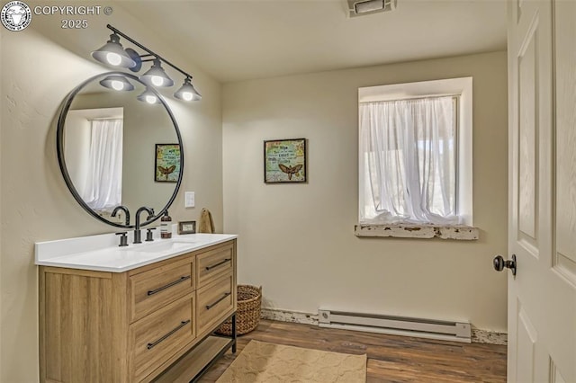 bathroom featuring visible vents, vanity, a baseboard heating unit, and wood finished floors