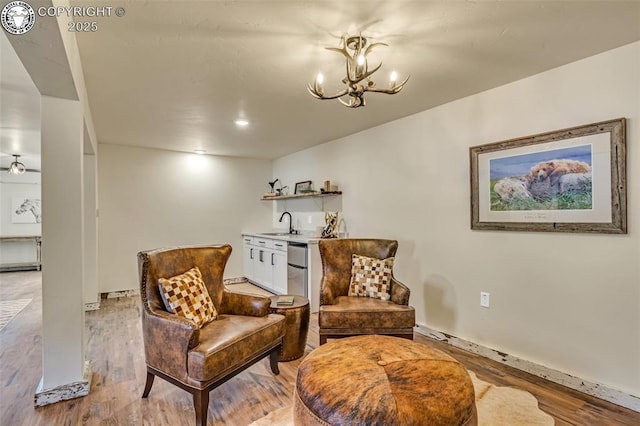 sitting room featuring indoor wet bar, light wood finished floors, and an inviting chandelier