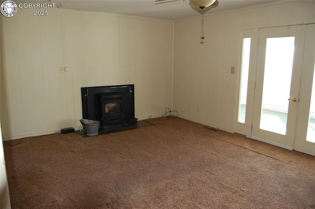 unfurnished living room featuring carpet flooring, a wood stove, and ceiling fan