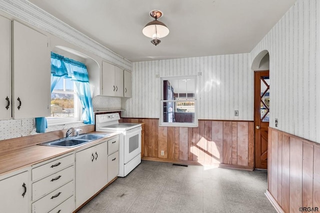 kitchen with wood walls, white cabinetry, sink, ornamental molding, and white electric range oven