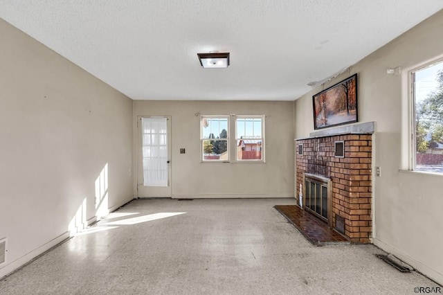 unfurnished living room with a healthy amount of sunlight, a brick fireplace, and a textured ceiling