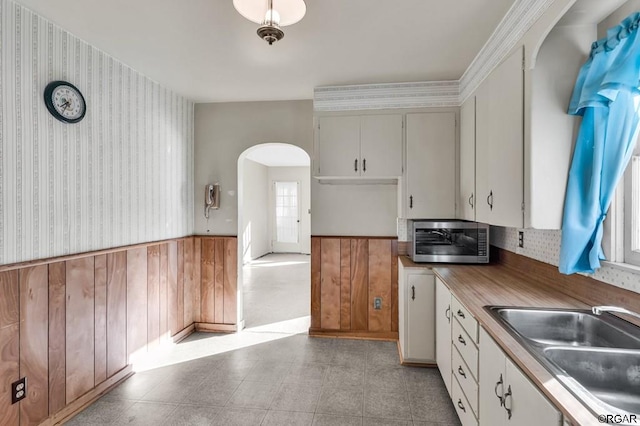 kitchen with white cabinetry, sink, crown molding, and wooden walls