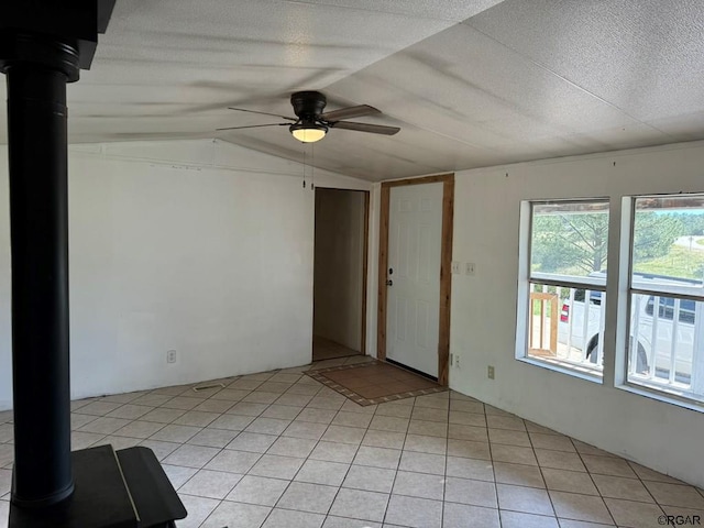 spare room with light tile patterned flooring, vaulted ceiling, a textured ceiling, a wood stove, and ceiling fan