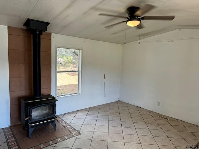 unfurnished living room with light tile patterned flooring, ceiling fan, vaulted ceiling, and a wood stove