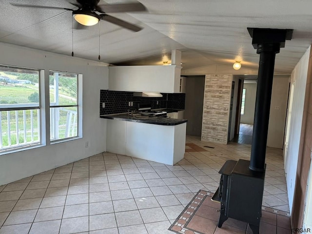 kitchen featuring white cabinetry, lofted ceiling, a wood stove, and backsplash