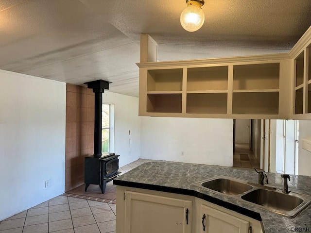 kitchen with light tile patterned flooring, sink, a wood stove, and a textured ceiling