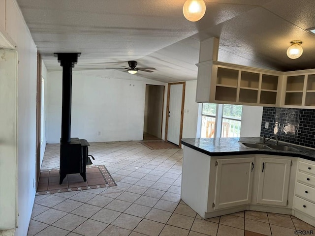 kitchen featuring sink, white cabinetry, backsplash, vaulted ceiling, and a wood stove