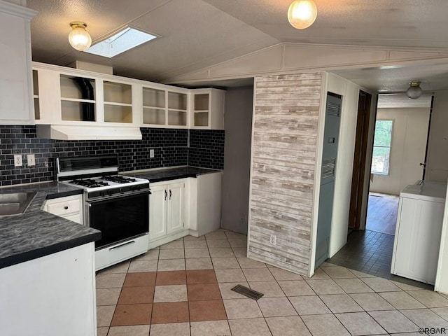 kitchen featuring lofted ceiling with skylight, washer / dryer, white cabinets, light tile patterned floors, and white gas stove