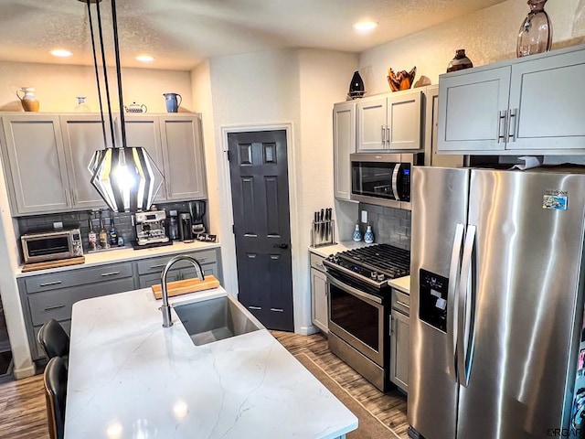 kitchen with pendant lighting, sink, gray cabinets, stainless steel appliances, and light stone countertops