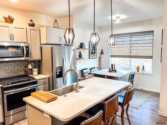 kitchen with appliances with stainless steel finishes, decorative light fixtures, a breakfast bar, and a center island with sink