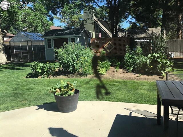 view of yard featuring an outbuilding, a greenhouse, a patio area, and fence