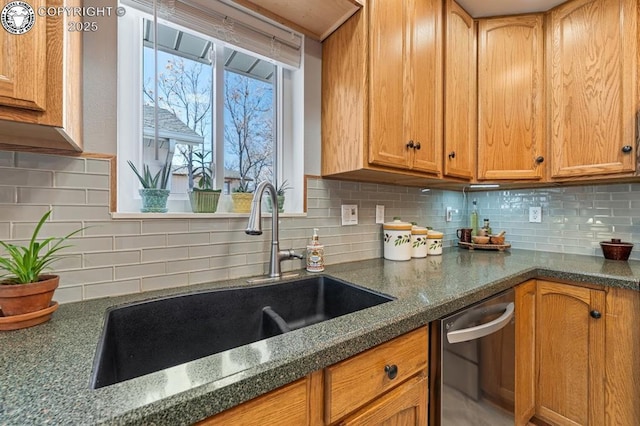 kitchen featuring dishwashing machine, dark stone counters, a sink, brown cabinets, and backsplash