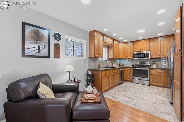 kitchen featuring a sink, stainless steel appliances, open floor plan, dark countertops, and tasteful backsplash