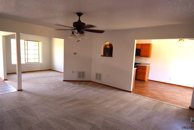 unfurnished living room with light carpet, ceiling fan, and a textured ceiling