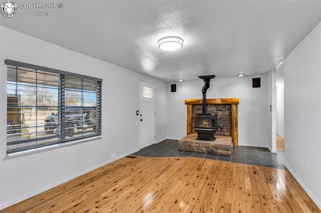 unfurnished living room featuring a healthy amount of sunlight, a wood stove, and dark hardwood / wood-style flooring