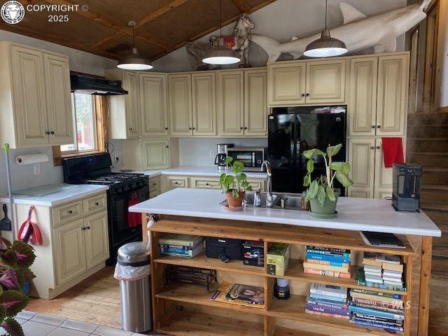 kitchen featuring lofted ceiling, range hood, black appliances, decorative light fixtures, and cream cabinetry