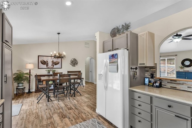 kitchen with arched walkways, tasteful backsplash, white refrigerator with ice dispenser, and gray cabinets