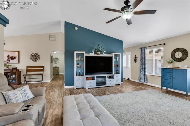 living area with vaulted ceiling, wood finished floors, arched walkways, and visible vents