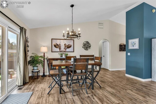 dining area with visible vents, wood finished floors, arched walkways, an inviting chandelier, and lofted ceiling