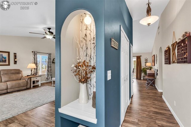 hall with wood finished floors, visible vents, baseboards, lofted ceiling, and arched walkways