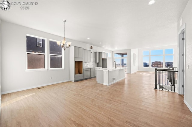 unfurnished living room featuring baseboards, light wood-style floors, a sink, and a notable chandelier