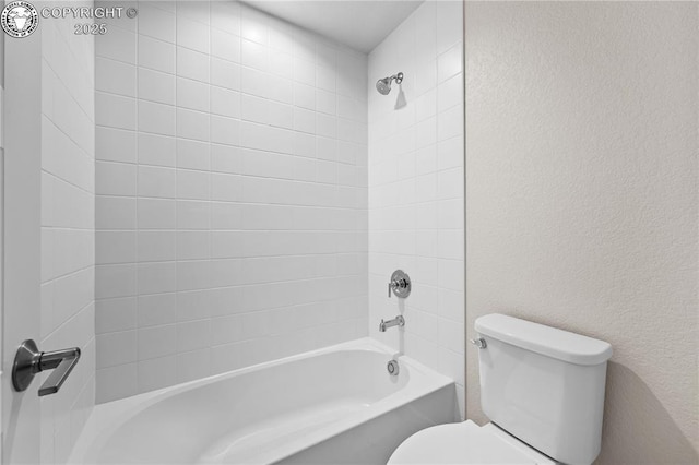 bathroom featuring toilet, shower / bath combination, and a textured wall