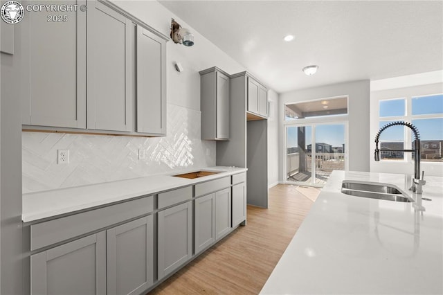 kitchen featuring recessed lighting, decorative backsplash, gray cabinetry, a sink, and light wood-type flooring