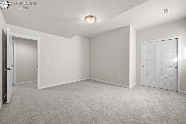 carpeted spare room with visible vents, a textured ceiling, and baseboards