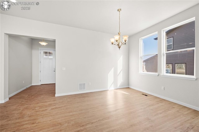 empty room with a notable chandelier, light wood finished floors, visible vents, and baseboards