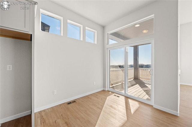 empty room with light wood-type flooring, visible vents, and baseboards