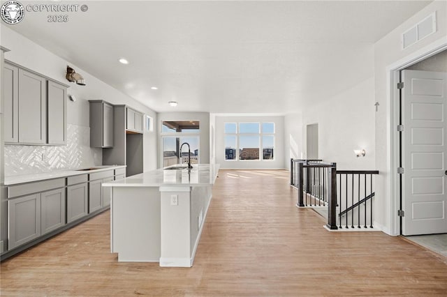 kitchen featuring light wood finished floors, visible vents, decorative backsplash, gray cabinets, and a sink