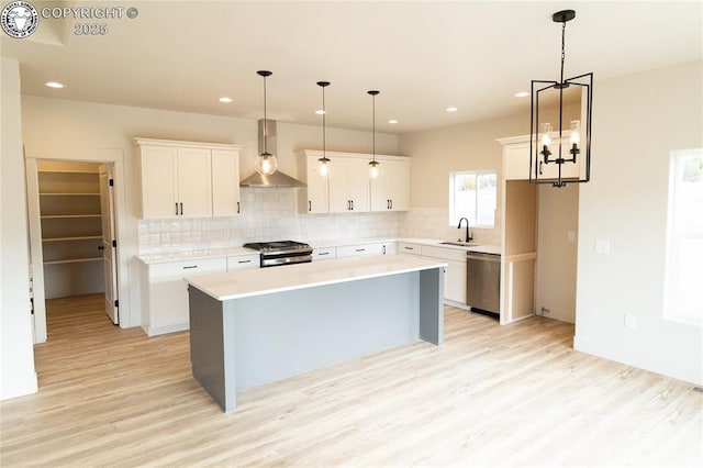 kitchen featuring a sink, a kitchen island, tasteful backsplash, appliances with stainless steel finishes, and wall chimney exhaust hood