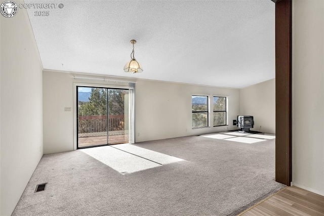 unfurnished living room with visible vents, a healthy amount of sunlight, a wood stove, and light colored carpet