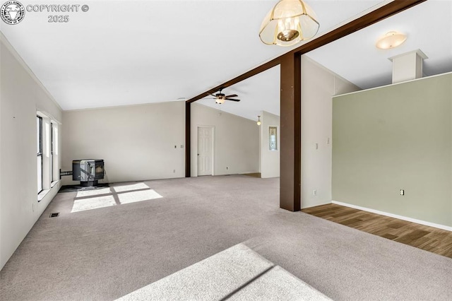 unfurnished living room with lofted ceiling with beams, carpet floors, a wood stove, and a ceiling fan