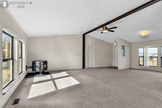 carpeted empty room featuring a wood stove, vaulted ceiling with beams, ceiling fan, and visible vents