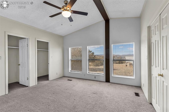 unfurnished bedroom featuring light carpet, lofted ceiling with beams, a textured ceiling, and two closets