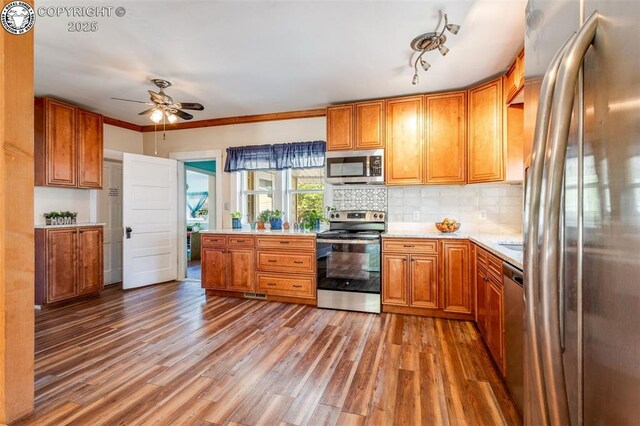 kitchen featuring crown molding, wood-type flooring, appliances with stainless steel finishes, ceiling fan, and backsplash