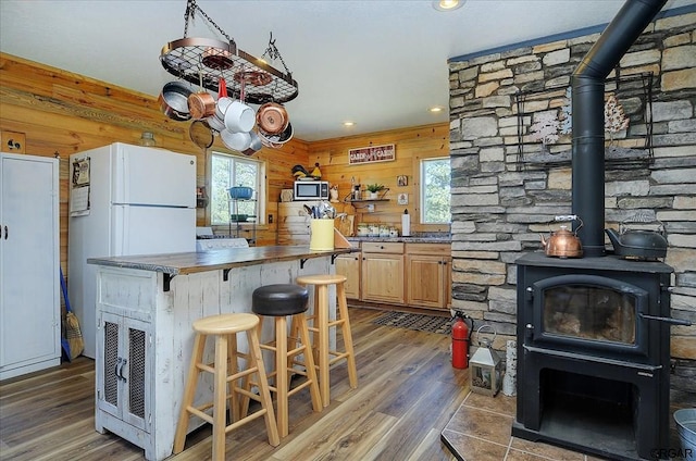 kitchen with a kitchen breakfast bar, wooden walls, light brown cabinetry, and a wood stove