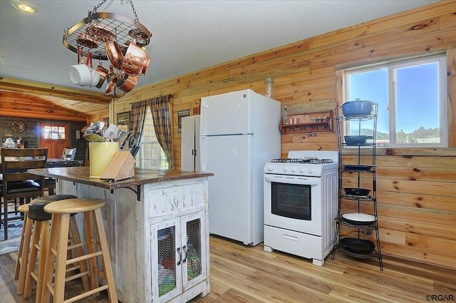 kitchen with white appliances, a kitchen bar, wooden walls, and light wood-type flooring