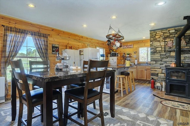 dining space with a wealth of natural light, light hardwood / wood-style floors, wooden walls, and a wood stove