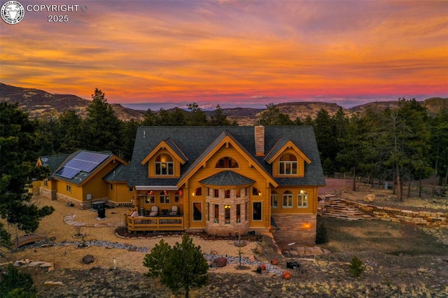 324 Elk View Ct, Canon City, CO 81212 - back of property at dusk featuring roof mounted solar panels, a mountain view, stone siding, and a chimney