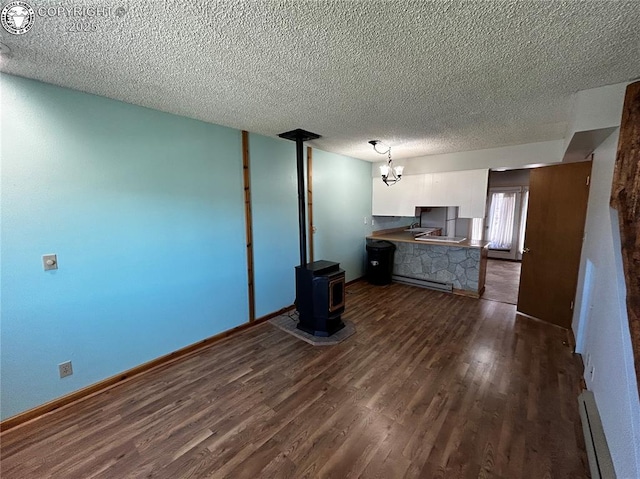 9 Granada Ct Unit 5, Westcliffe, CO 81252 - unfurnished living room featuring baseboard heating, dark wood-style flooring, a textured ceiling, a chandelier, and a wood stove