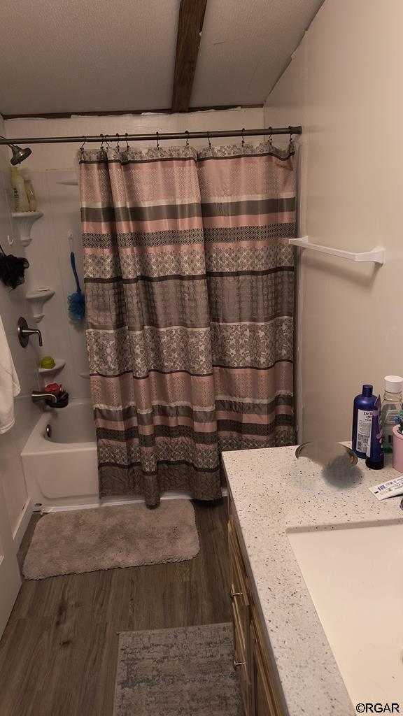 bathroom with wood-type flooring, shower / bathtub combination with curtain, vanity, and a textured ceiling