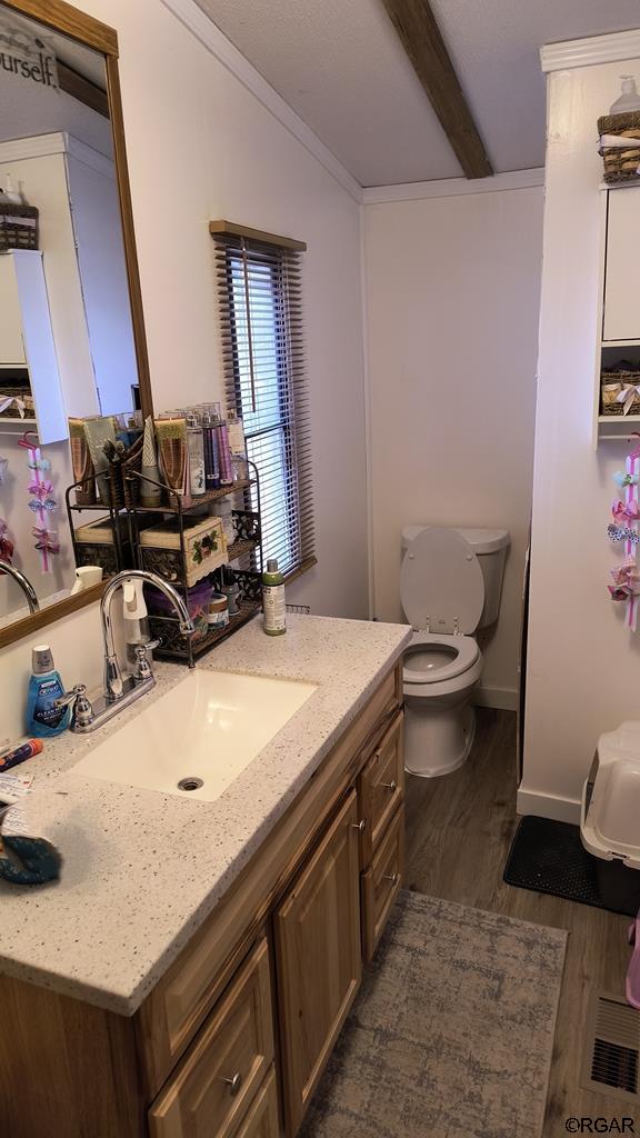 bathroom featuring hardwood / wood-style floors, beam ceiling, vanity, ornamental molding, and toilet