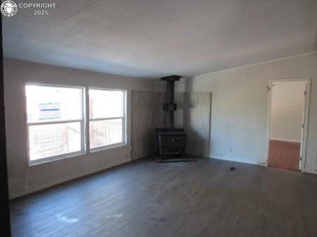 unfurnished living room featuring a wood stove, crown molding, and wood finished floors