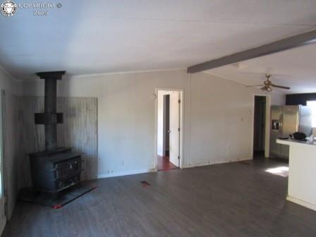 unfurnished living room with a wood stove, vaulted ceiling with beams, a ceiling fan, and wood finished floors