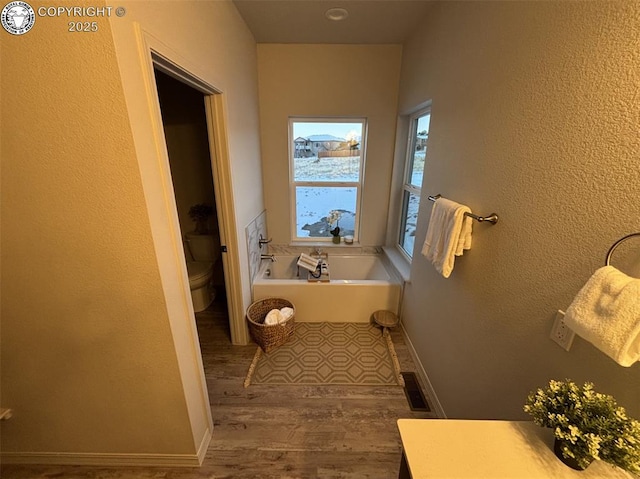 bathroom with wood-type flooring, toilet, and a bath